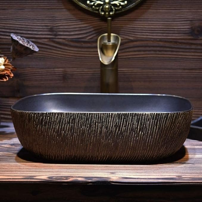 Vasque à poser vintage en céramique noire mate avec finition texturée effet bronze et robinet cascade doré brossé.